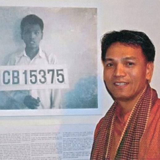 <span style="color: #000000 !important;font-size: 14pt">Sayon, now an adult and American citizen, poses with his refugee camp identification photo at the "More Than a Number" photo exhibit.</span>